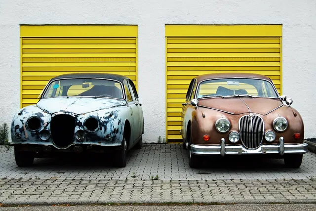Du egalaj aŭtoj ( Jaguar Mark II — luksa “klasika” modelo, ĉ. 1960) antaŭ egalaj flavaj garaĝpordoj sur truotuaro el betonaj kaheloj: Tiu maldekstre kun metalpolura riparo antaŭ ol farbado, sen ĥromaĵoj, tiu dekstre jam preta kun helbruna farbtego. Garage door service marketing: channels, reviews, and rules